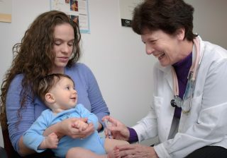 Medic care examinează un bebeluș ținut în brațe de mama lui