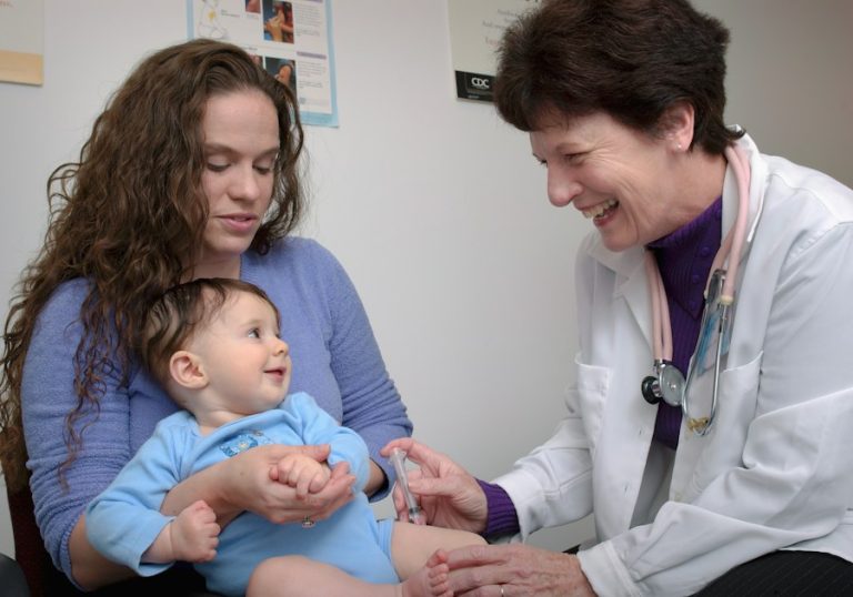 Medic care examinează un bebeluș ținut în brațe de mama lui