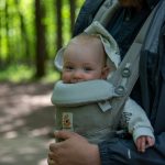Bebeluș purtat în marsupiu, cu picioarele depărtate, în timpul unei plimbări