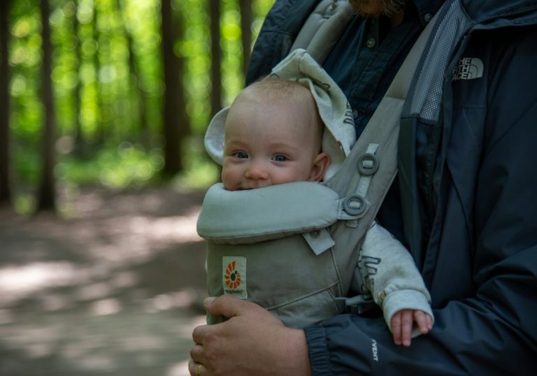 Bebeluș purtat în marsupiu, cu picioarele depărtate, în timpul unei plimbări