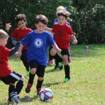 Copii care joacă fotbal pe gazon, într-un meci între echipe de juniori