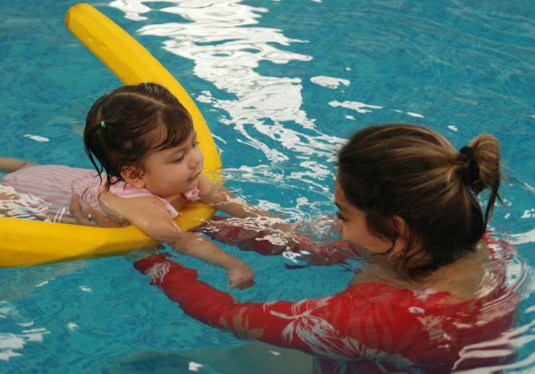 Fetiță care învață să înoate în piscină, ajutată de mama ei