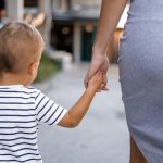 Copil mic care merge ținut de mână de mama lui pe stradă