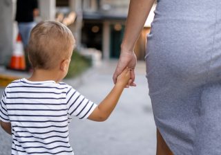 Copil mic care merge ținut de mână de mama lui pe stradă