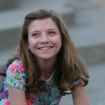 Adolescentă care zâmbește, stând pe trepte în aer liber