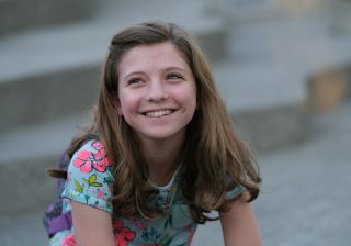 Adolescentă care zâmbește, stând pe trepte în aer liber