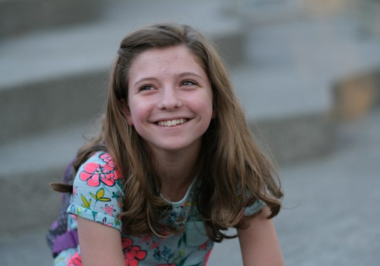 Adolescentă care zâmbește, stând pe trepte în aer liber